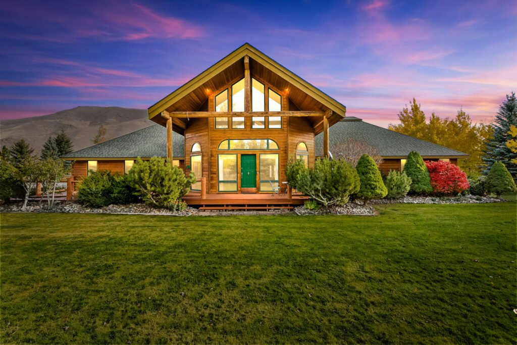 Timber home at twilight with lit windows and a wide lawn