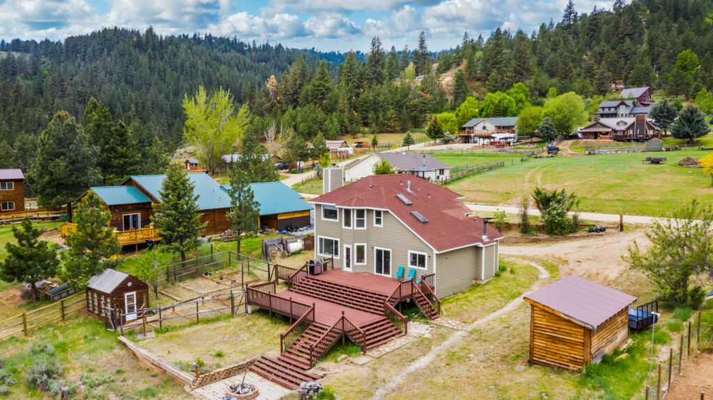 Mountain home with red roof, decks and outbuildings among pines